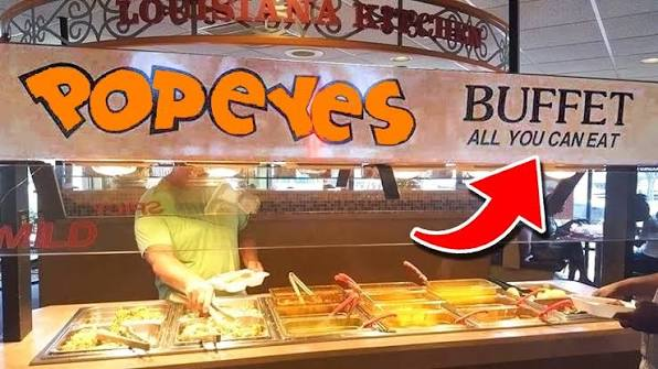 A Popeyes all-you-can-eat buffet counter with trays of food beneath a Louisiana Kitchen sign