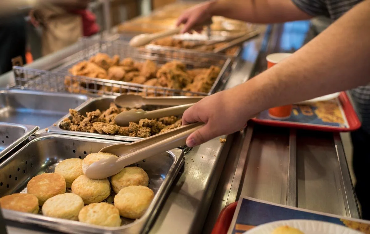 Diners using tongs to serve fried chicken and biscuits from a Popeyes buffet
